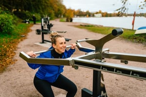 En glad kvinna använder en knäböjsmaskin på ett utegym i Stockholm under hösten.
