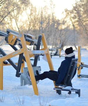 En man sitter i en gul benpress på ett utegym från Omnigym under en kall vinterdag